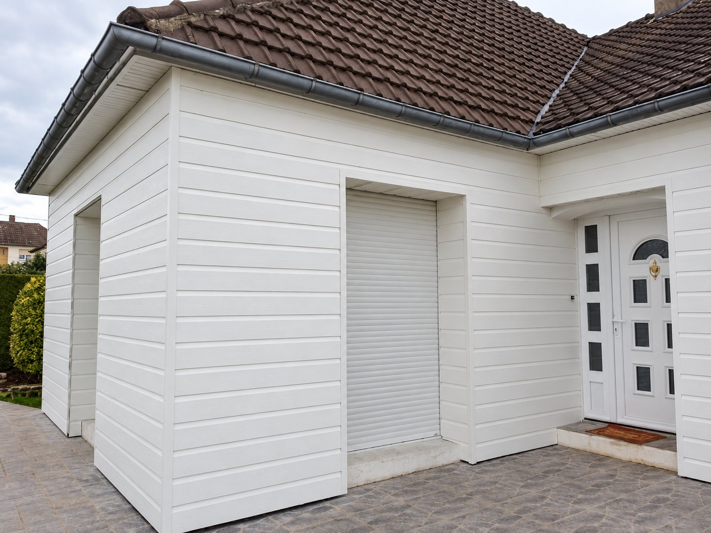 Façade d'une maison recouverte de bardage PVC blanc, avec un volet roulant fermé et une porte d'entrée blanche vitrée.